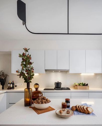 White kitchen island styled with amber bottles, walnuts, and bread under a black linear pendant light