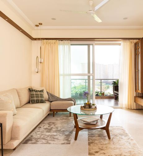 Beige sectional sofa and round glass coffee table facing balcony with city view