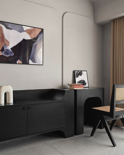 Black sculptural sideboard with arched cutout beside cane chair and abstract painting on plaster wall