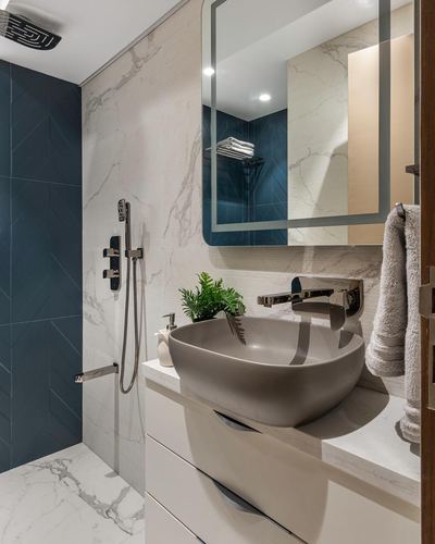Modern bathroom with teal tiled shower, veined stone walls, backlit mirror and matte grey vessel sink