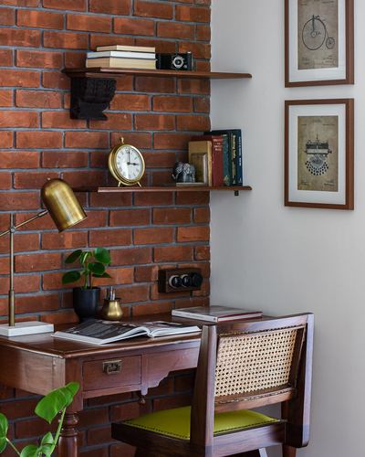 Study nook with brick wall, wood shelves, brass lamp, cane chair and vintage desk