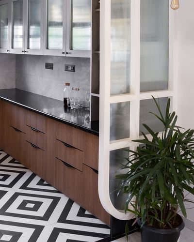Kitchen corner with wood cabinets, black counter, and a curved fluted glass partition beside a plant.
