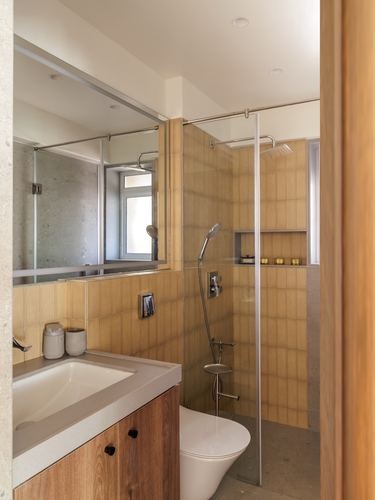 Minimalist bathroom with ribbed tan tile shower, wood vanity, and wall-mounted toilet behind glass partition.
