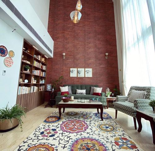 Double-height living room with red brick wall, green sofa, and colorful floral rug