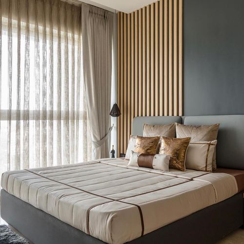 Bedroom with upholstered grey headboard, gold cushions, and fluted wood accent wall beside sheer curtains