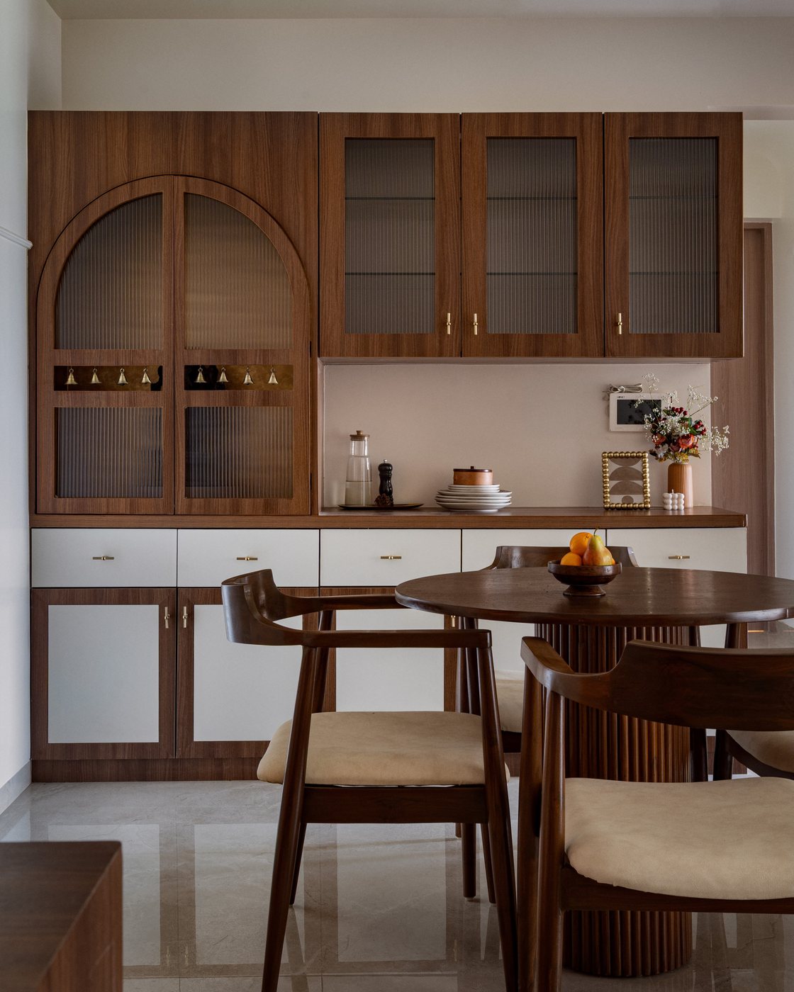 Walnut dining cabinet with arched glass door beside round table and cane-backed chairs