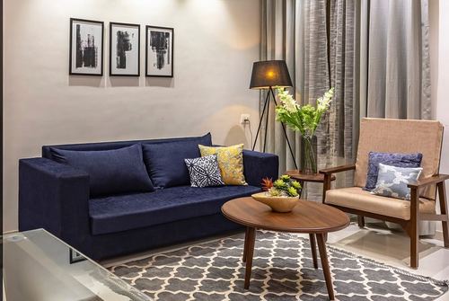Living room with navy velvet sofa, wooden coffee table, cane armchair and patterned rug