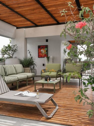Covered terrace with sage striped sofa, lounge chair, potted plants and slatted wood ceiling