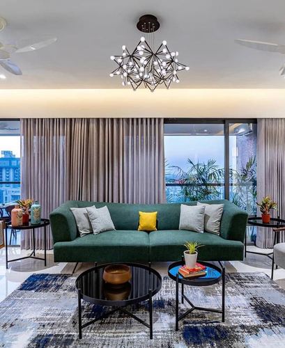 Green velvet sofa with round black coffee tables under a star-shaped chandelier, city view beyond