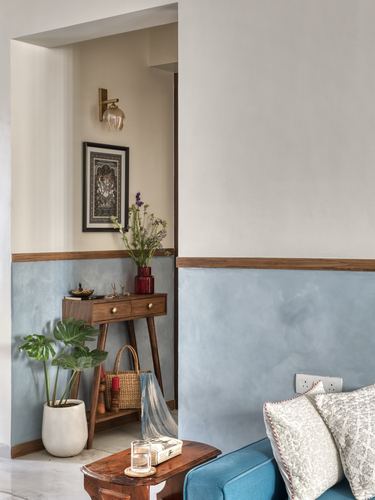 Foyer nook with blue dado wall, wooden console table, framed art, and monstera plant