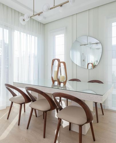 Dining room with glass-top table, curved wood chairs, round mirror and sheer curtained windows