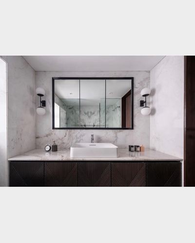 Symmetrical marble-look bathroom vanity with black-framed mirror, globe sconces, and dark ribbed cabinetry
