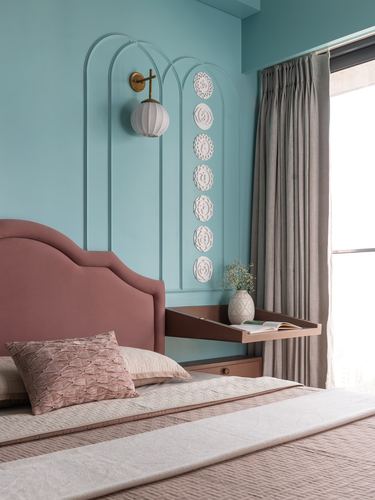 Teal bedroom wall with arched moulding, brass sconce, and pink upholstered headboard with fold-out desk
