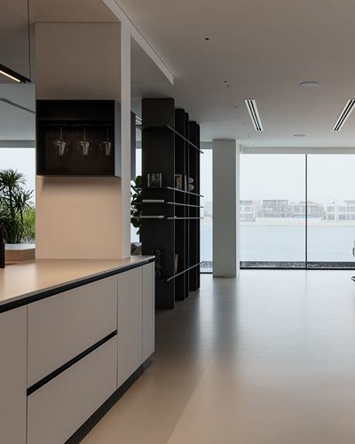 Minimalist kitchen island with dark shelving unit and waterfront view through glass wall