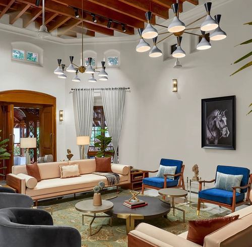 Double-height living room with exposed wood truss ceiling, brass chandeliers, blush sofa and blue velvet armchairs