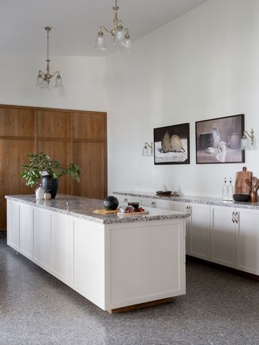 White kitchen island with terrazzo top, wood cabinetry wall, and framed still-life art above counter