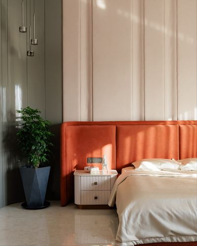 Bedroom corner with orange velvet headboard, cream paneled wall, white nightstand and potted plant