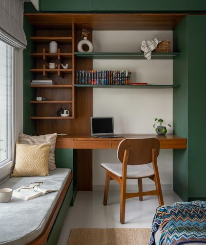 Green built-in study nook with wooden desk, open shelves, and window seat with cushions
