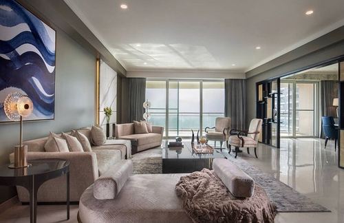 Neutral-toned living room with beige sofas, round ottoman, and floor-to-ceiling glass doors to balcony