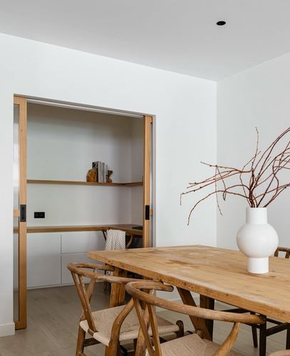 Dining table with wishbone chairs beside a reeded glass pocket door opening to a built-in study nook