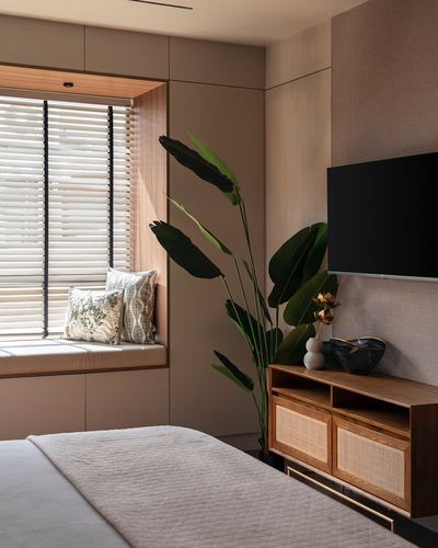 Bedroom corner with wood window seat, large plant, and cane-front TV console