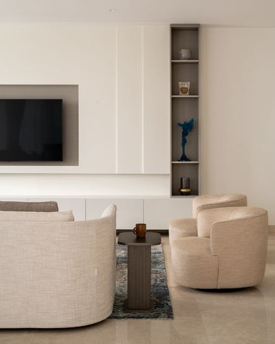Minimalist beige living room with curved sofas, swivel chairs, and a display niche beside a wall-mounted TV
