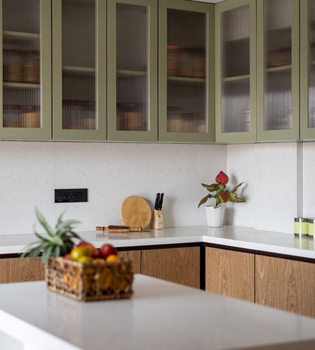 Kitchen corner with sage green fluted-glass cabinets over wood-toned lower units and stone counters