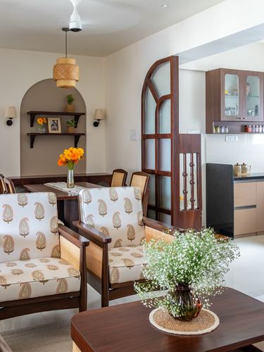 Living and dining area with arched wood partition opening to kitchen, paisley armchairs, floral centerpieces