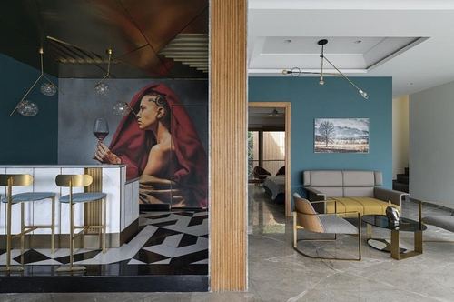 Split view of a home bar with mural and a teal-walled living room beyond a fluted wood column