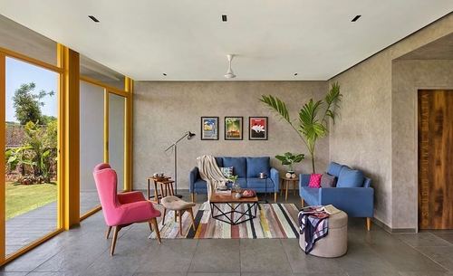 Living room with blue sofas, pink armchair, striped rug and yellow-framed glass doors to garden