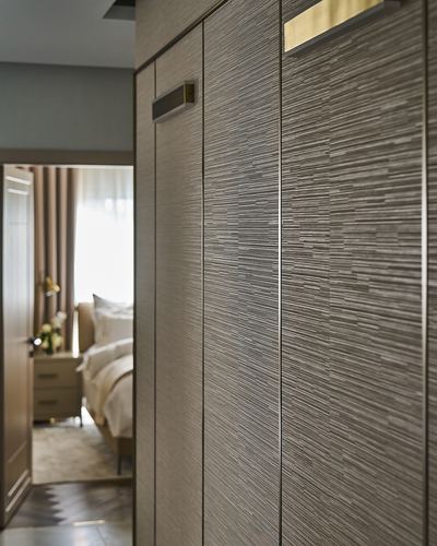 Close-up of ribbed wood wardrobe doors with brass handles, doorway open to bedroom beyond