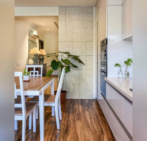 Kitchen with white glossy cabinetry, wood-look tile floor, and patterned tile column opening to dining area
