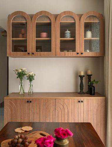 Wooden arched glass cabinet above a carved sideboard styled with flowers and candles