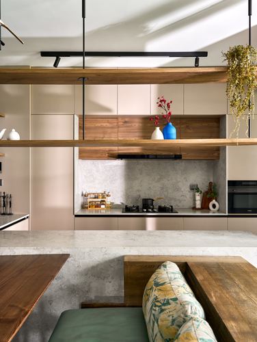 Beige kitchen with wood floating shelves, stone backsplash, and a walnut bench in foreground