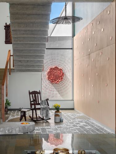 Double-height foyer with concrete staircase, rocking chair, patterned stone floor and textured pink wall
