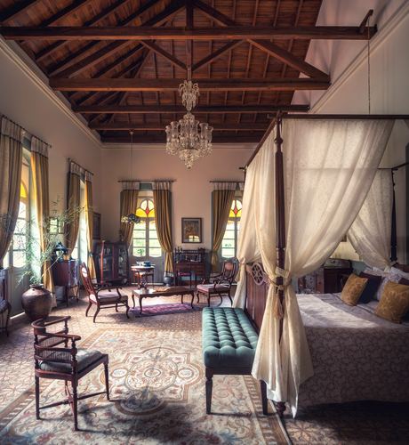 Colonial bedroom with exposed wood trusses, canopy bed, crystal chandeliers, and stained-glass windows