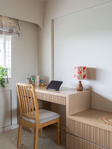 Light wood study desk with fluted paneling, chair, lamp, and window in a minimalist corner