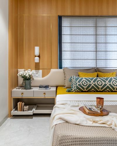 Bedroom corner with wood-paneled headboard wall, mustard and teal bedding, and a two-drawer nightstand.