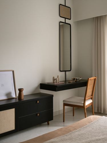 Black floating desk and cane chair beneath a tall leaning mirror in a neutral bedroom corner