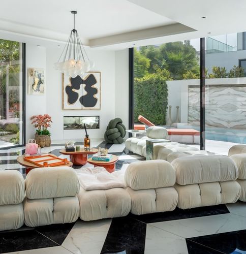 Living room with cream tubular sofa on checkerboard marble floor, glass walls open to garden and pool
