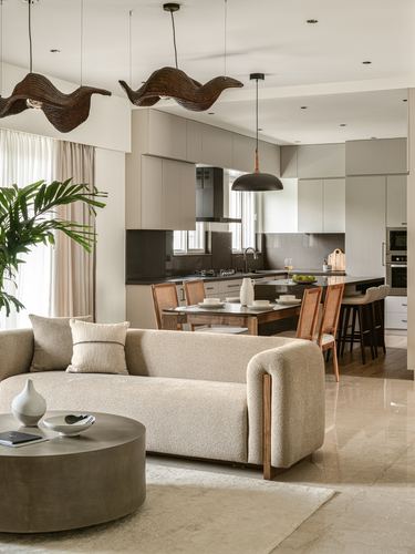 Open-plan living and dining space with curved beige sofa, sculptural pendant lights, and kitchen beyond