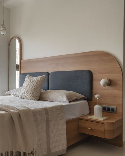 Bed with curved wood headboard, blue upholstered panels, floating nightstand and arched mirror