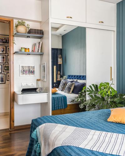 Bedroom with blue upholstered bed, mirrored wardrobe reflecting fluted headboard wall, and study nook