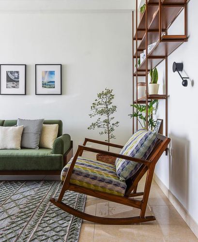 Wooden rocking chair with patterned cushions beside green sofa and open wood shelving unit