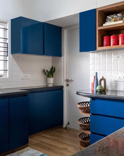 Navy blue kitchen with white tiled backsplash, wood open shelving and wicker baskets under counter
