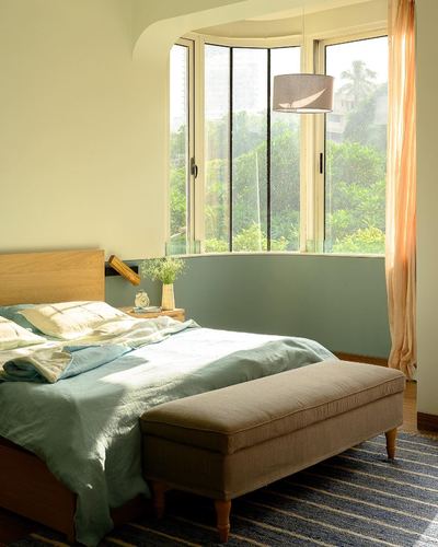 Bedroom with curved bay window overlooking greenery, wooden bed, and upholstered bench at foot