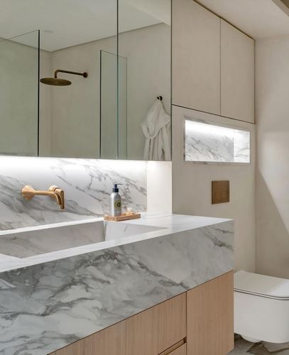 Marble vanity and backsplash bathroom with brass fixtures and lit niche