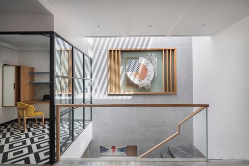 Staircase landing with wooden framed art panel, glass railings, and patterned floor under striped light