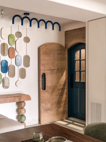 Entryway with arched teak door, mirror collage wall, and stacked-ball console leg leading to a teal front door