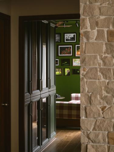View through a wooden doorway past a stone pillar into a green bedroom with framed photographs and a checkered bedspread